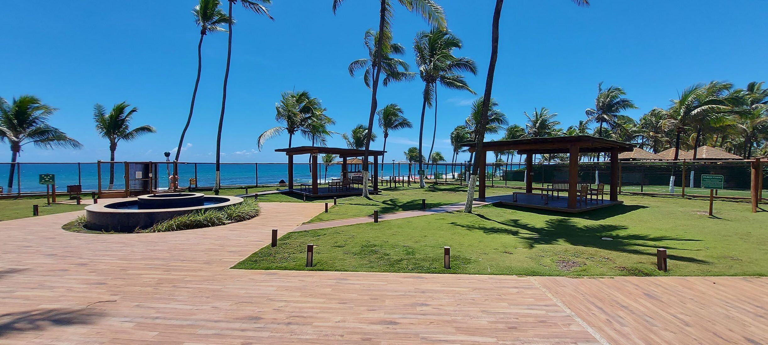 Um resort à beira-mar com palmeiras, um deck de madeira e um espelho d'água circular.