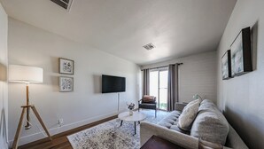 Ein Wohnzimmer mit einer Couch, einem Couchtisch, einer Lampe, einem Fernseher und einem Fenster mit Vorhängen.