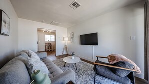 Ein Wohnzimmer mit einer Couch, einem Couchtisch, einem Fernseher und einem kleinen Tisch mit einer Lampe.
