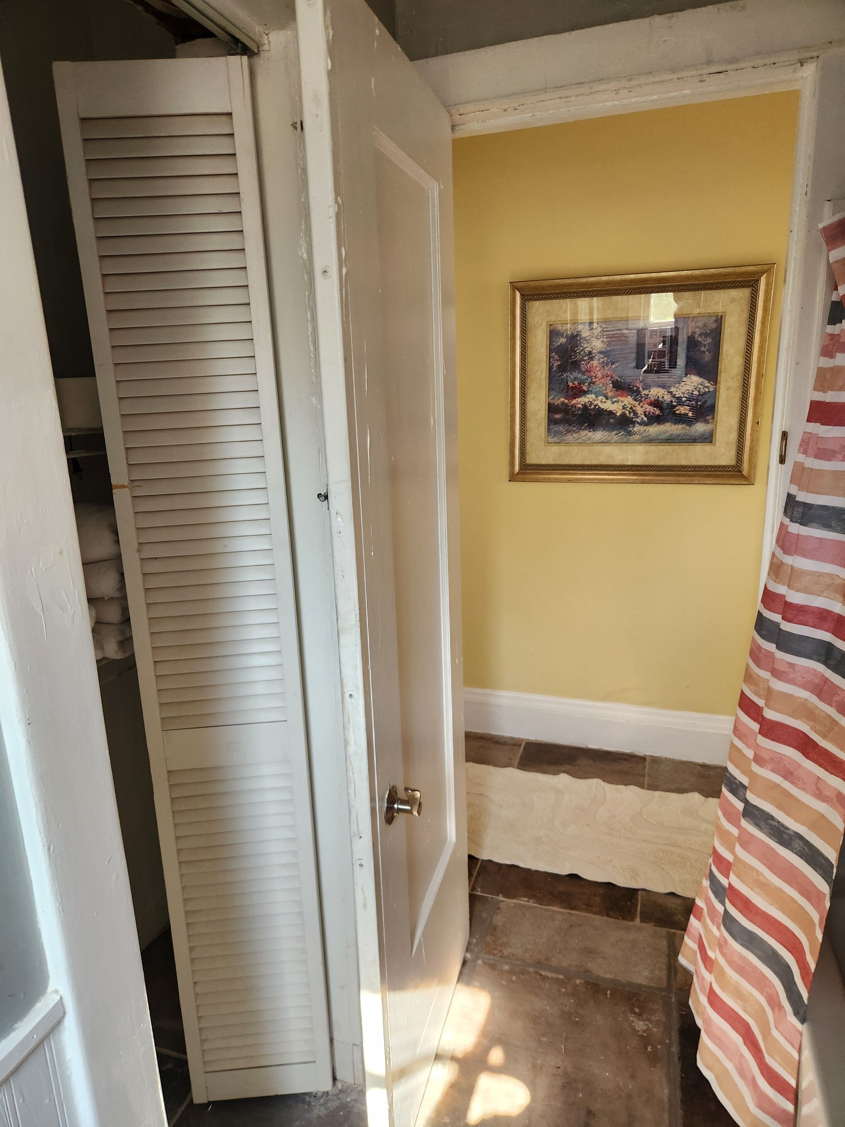 A hallway with a white door, a framed picture on the wall, and a striped curtain.