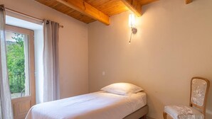 Un dormitorio con una cama, una silla, un ventanal con cortinas y una lámpara de pared.