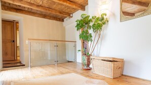 Una habitación con techo de madera, puerta de vidrio, planta en maceta, cesta de mimbre y un pouf tejido.