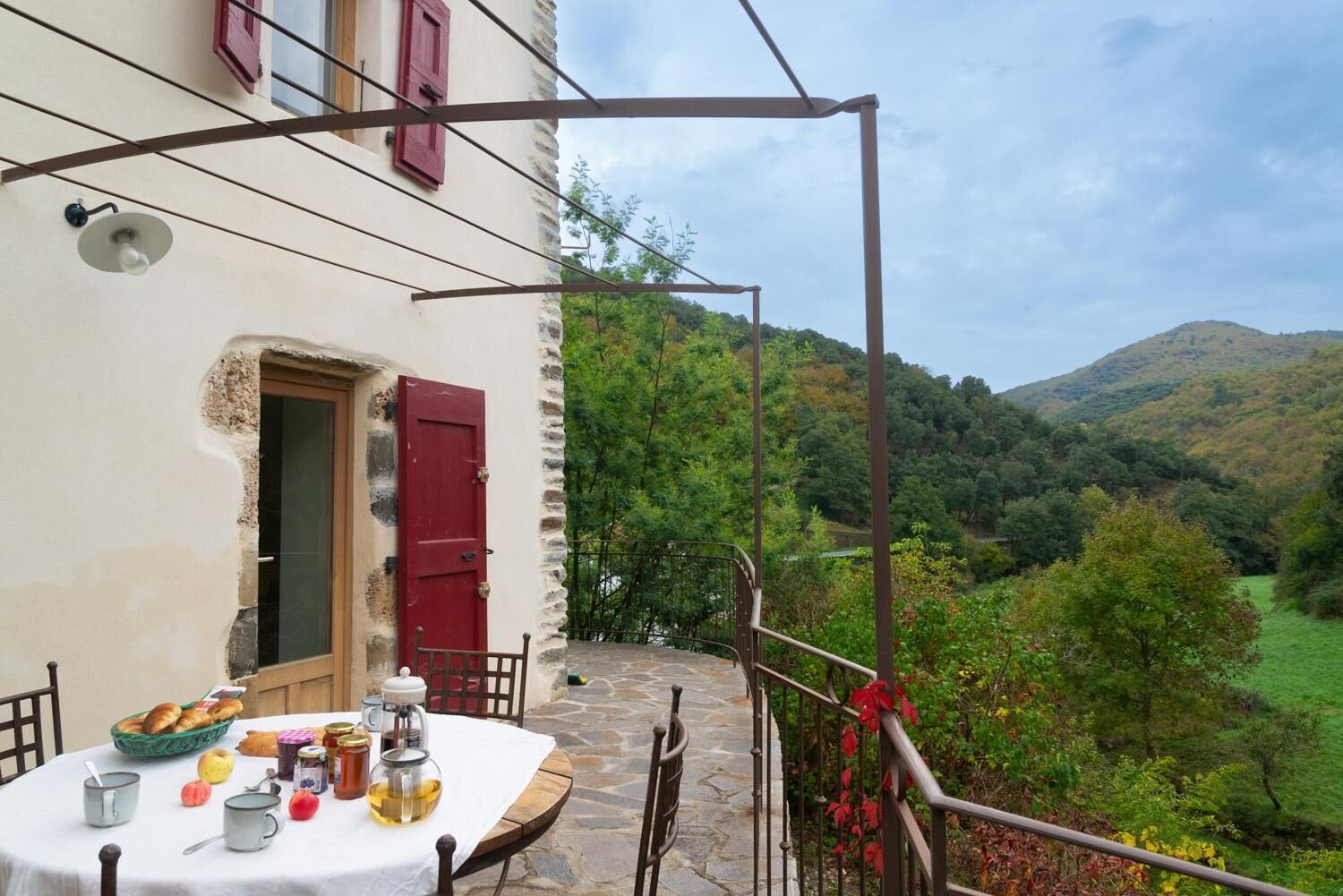Una mesa de piedra con alimentos para el desayuno, una puerta roja y vistas a un valle verde.