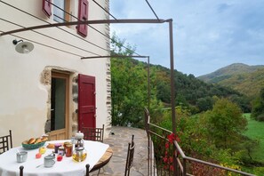 A stone table with breakfast items, a red door, and a view of a green valley. - EcoGîte Cévénola (sleeps 3) (MOLEZON)