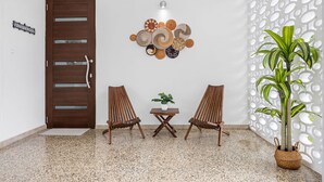 Ein Zimmer mit Holztür, zwei Korbstühlen, einem kleinen Tisch mit Pflanze und einem Blumentopf.