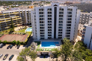 A high-rise hotel with multiple balconies, a swimming pool, and a parking area. - Apartment Tália with Pool by Centralgarve (Loulé)
