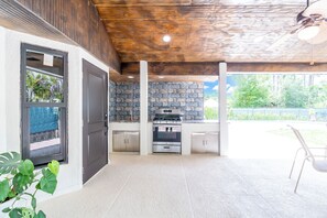 An outdoor kitchen with a stone backsplash, a built-in oven, and a ceiling fan.