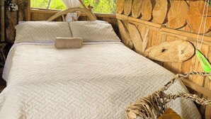 A wooden cabin bedroom with a bed, a window with a curtain, and a stone wall.