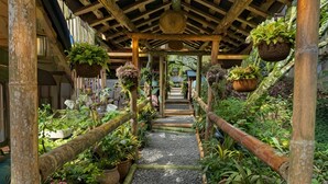 A covered walkway with a gravel path, bamboo railings, and hanging planters with various plants.