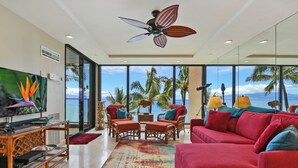 A modern living room with a large red sofa, a television, and a ceiling fan. - ~MAHANA 505~Ocean Front Condo with A/C & Beautiful Island Views in Kaanapali (Lahaina)
