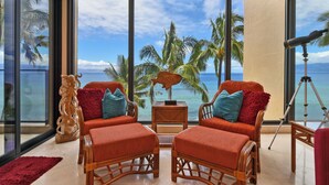 A room with a large window overlooking the ocean, featuring wicker furniture and a red rug. - ~MAHANA 505~Ocean Front Condo with A/C & Beautiful Island Views in Kaanapali (Lahaina)