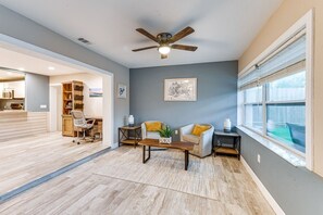 Ein Wohnzimmer mit Deckenventilator, einer Couch, einem Couchtisch und einem Fenster mit Jalousien.