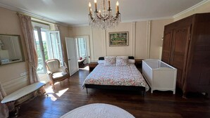 A bedroom with a bed, a crib, a chandelier, a chair, a desk, a mirror, and a painting on the wall. - La demeure aux Lilas a large stone mansion (Cirey-sur-Blaise)