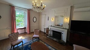 A living room with a fireplace, a chandelier, and a television. - La demeure aux Lilas a large stone mansion (Cirey-sur-Blaise)