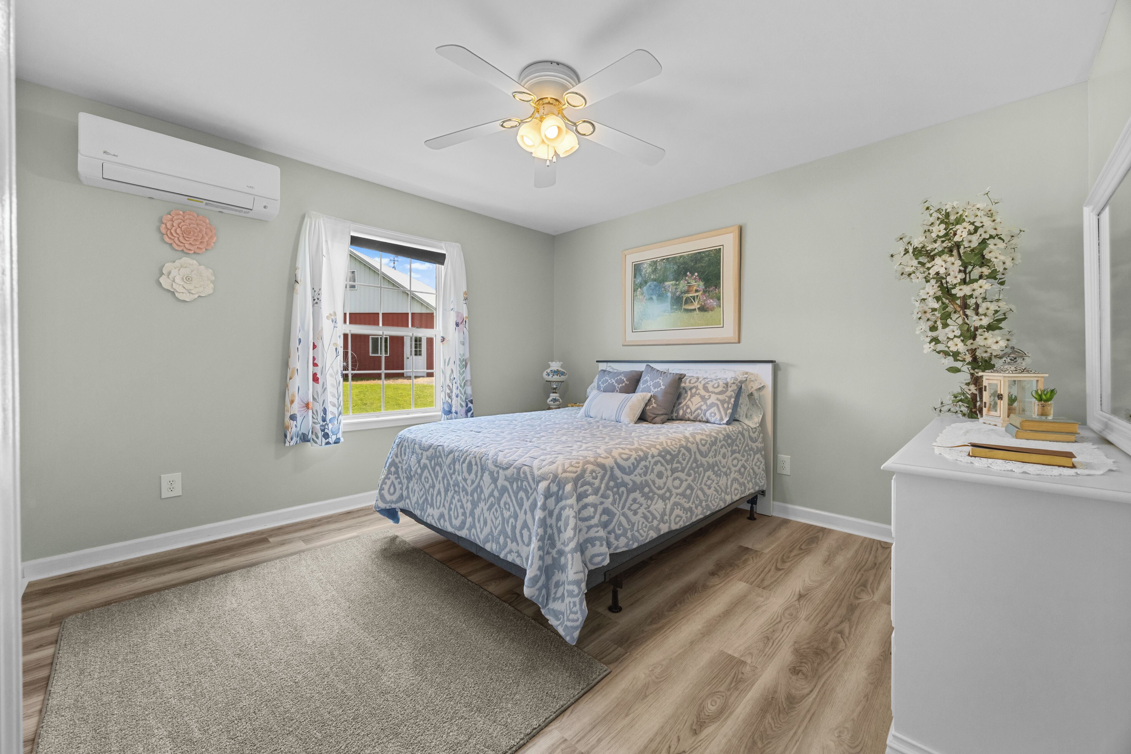 A bedroom with a bed, a nightstand, a window with curtains, a ceiling fan, and a wall-mounted air conditioner.