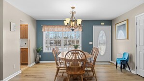 Una sala da pranzo con un tavolo e sedie in legno, un lampadario, una finestra con vista e una porta con pannello di vetro decorativo.