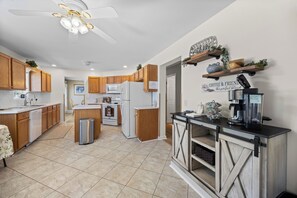 A modern kitchen with wooden cabinets, a central island, a coffee station, and a ceiling fan.