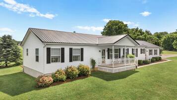 A single-story white house with a porch, surrounded by a well-maintained lawn and trees.