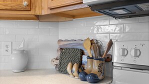Una cucina con piastrelle bianche, mobili in legno, un fornello bianco e un oggetto decorativo lavorato a maglia sul ripiano.