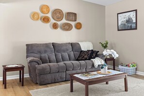 A living room with a grey sofa, a coffee table with magazines, a small side table, and decorative baskets on the wall.