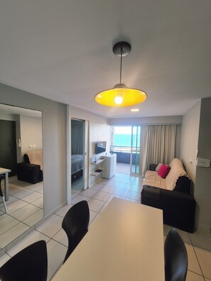 A modern living room with a dining area, a sofa set, a TV, and a balcony with a view. - Beach Class Fortaleza 1001, Ocean View, up to 4 guests. (Fortaleza)