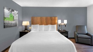 Hotellihuone, jossa on suuri sänky, kaksi yöpöytää valaisimineen, tuoli ja taideteos seinällä.