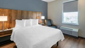 Hotellihuone, jossa on suuri sänky, yöpöytä, tuoli, ikkuna, josta on näkymä, ja seinälle asennettu ilmastointilaite.