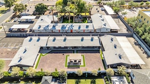 Ein weiter Blick von oben auf ein großes Gebäude mit mehreren Parkplätzen, einem zentralen Innenhof mit Sitzgelegenheiten und umgebender Bepflanzung.