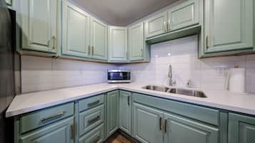 A kitchen with teal cabinets, white countertops, a stainless steel sink, and a microwave.
