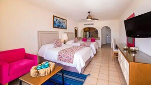 A hotel room with a bed, a TV, a kitchenette, and a pink sofa. - Cabo Beachfront Escape with Stylish Studio & Resort Pool Access (Cabo San Lucas)