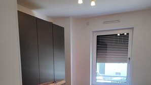 A bedroom with a bed, a wardrobe, a nightstand, a window with blinds, and a ceiling light fixture. - Modern apartment for families with small children. U1 within walking distance (Nürnberg)