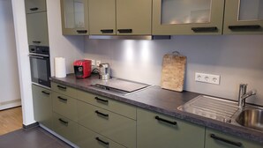 A modern kitchen with green cabinets, a built-in oven, a coffee maker, a cutting board, and a sink. - Modern apartment for families with small children. U1 within walking distance (Nürnberg)