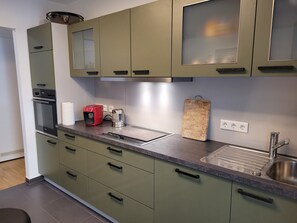 Eine moderne Küche mit grünen Schränken, einem eingebauten Backofen, einer Kaffeemaschine, einem Schneidebrett und einer Spüle.