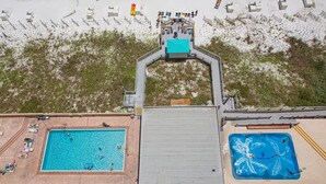 Vista aérea de um resort com duas piscinas, área de praia e uma galeria coberta.