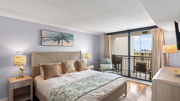 Quarto de hotel com uma cama, duas mesas de cabeceira com luminárias, uma cadeira, uma varanda com vista e um quadro na parede.