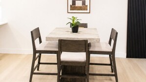 A dining area with a wooden table, four chairs, a potted plant, and a framed picture on the wall. - Modern Dallas Retreat • Golf • Speakeasy• Fire Pit (Dallas)