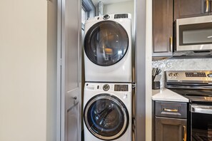 A compact laundry area with a front-loading washer and dryer, a microwave, and a stainless steel oven. - Modern 2BR : Historic Lebanon • Sleeps 4 (Lebanon)