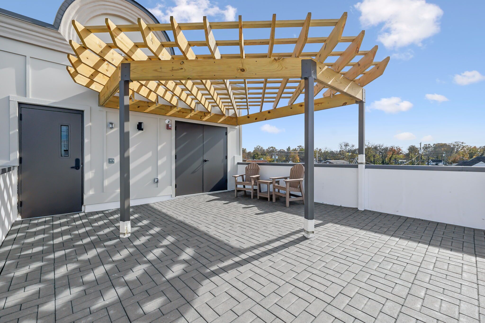 Uma área externa coberta com pérgola de madeira, uma porta e um espaço para sentar.