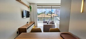Ein modernes Wohnzimmer mit Fernseher, einem Holztisch, einer Couch und einem Balkon mit Blick auf die Stadt.