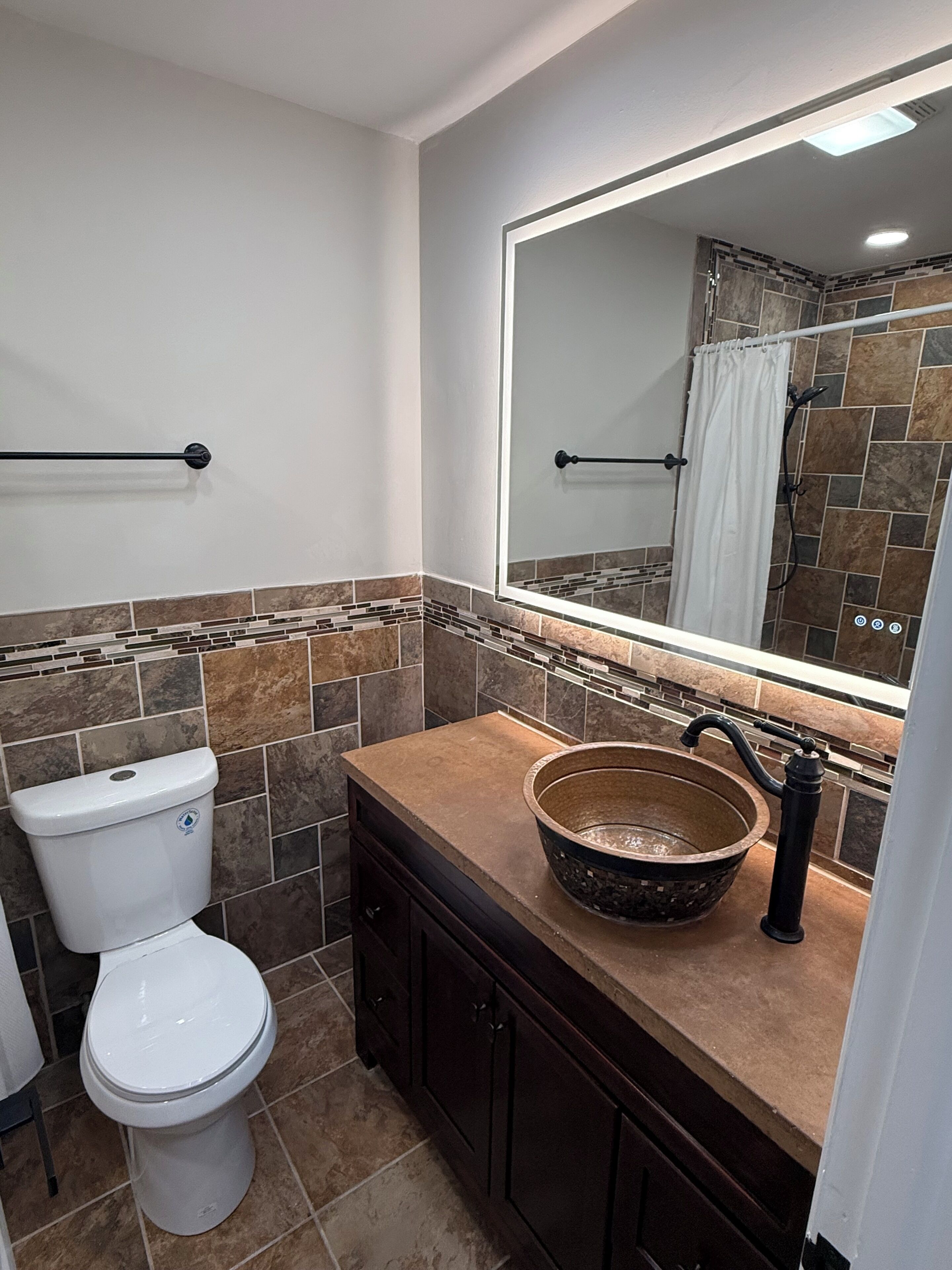A bathroom with a toilet, a sink with a basin, a mirror, and a shower area.