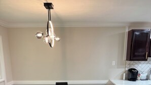 Een eetgedeelte met een rechthoekige tafel en zwarte stoelen, een hanglamp, en een keuken met donkere kasten en een wit aanrecht.