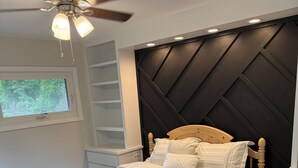 Een slaapkamer met een bed, een plafondventilator, een raam en een inbouwplank.