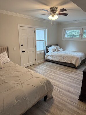 A bedroom with two beds, a ceiling fan, a window, and a door.