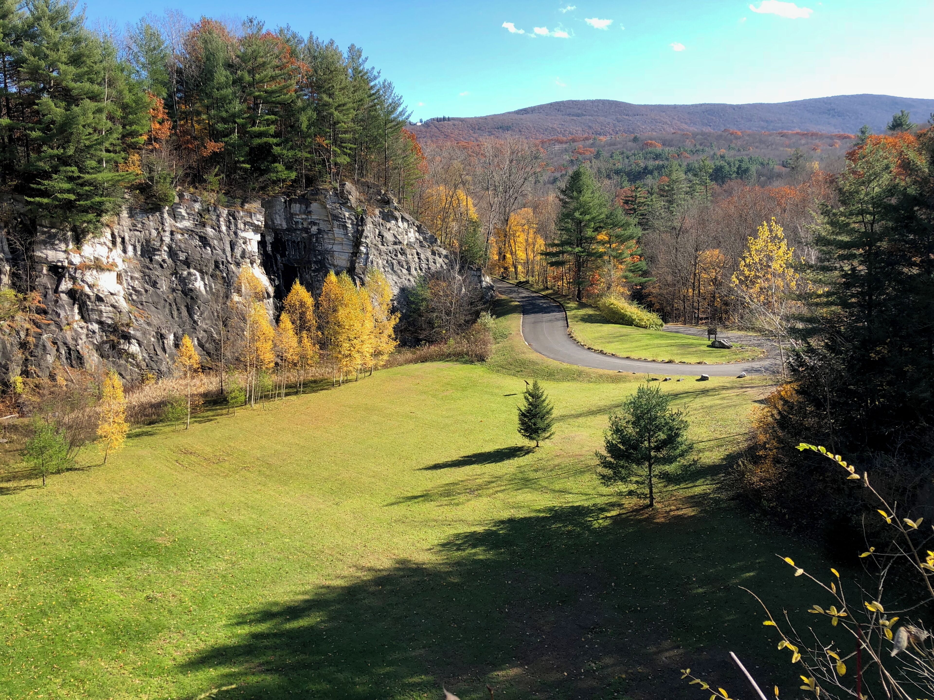 A scenic landscape with a winding road, grassy areas, and a rocky cliff.