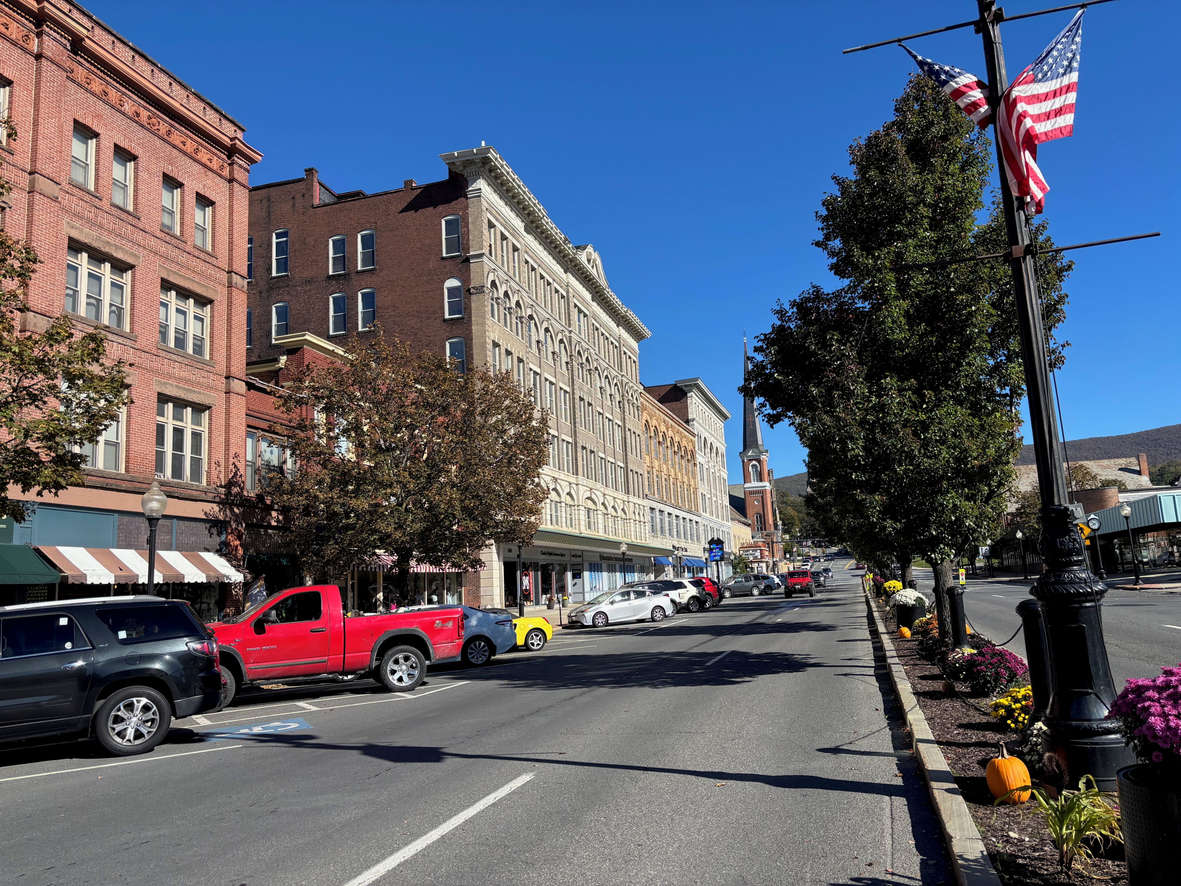 A street lined with historic buildings, a red pickup truck parked on the side, and a row of parked cars.
