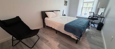 A bedroom with a bed, a chair, a desk, and a window.