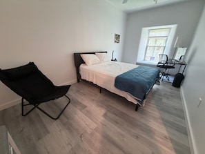 Un dormitorio con cama, una silla, un escritorio y un ventanal.