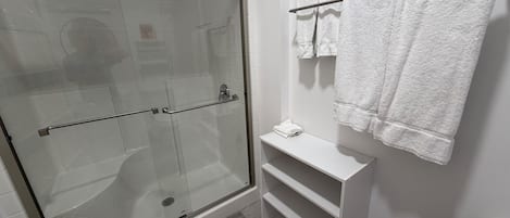 Un baño moderno con cabina de ducha de vidrio, paredes con azulejos blancos, un perchero blanco y un estante blanco.