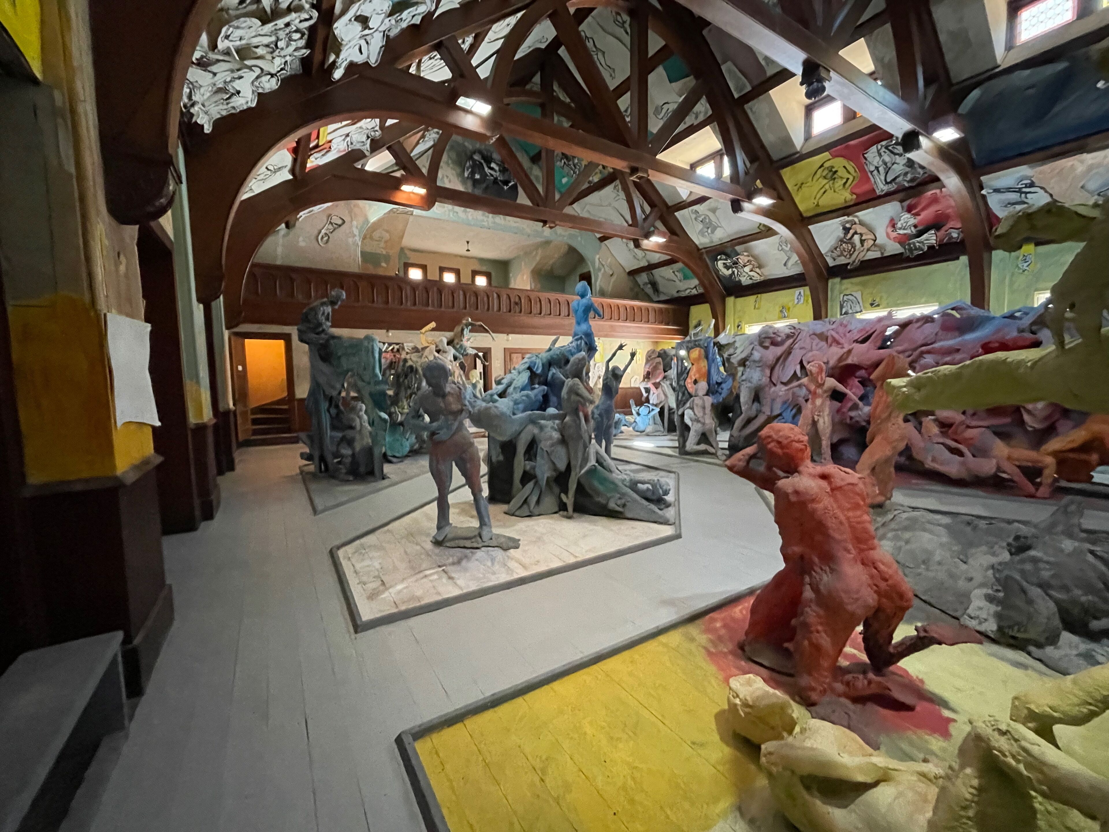 An interior with a high ceiling, wooden beams, and a central sculpture surrounded by smaller artworks.