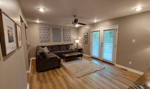 Ein Wohnzimmer mit Sofa, Couchtisch und Teppich. Es gibt Deckenleuchten und einen Deckenventilator.